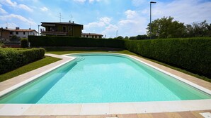 Ein rechteckiger Pool mit klarer, blauer Wasseroberfläche, umgeben von einer niedrigen Hecke und einem gepflasterten Weg.