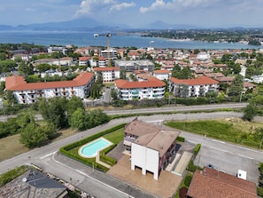 A residential area with a swimming pool, a road, and a distant view of a body of water and mountains.