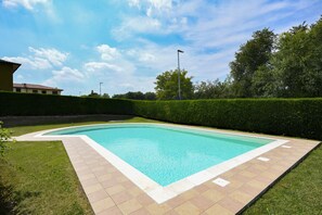 Ein rechteckiger Pool mit einer gefliesten Umrandung, umgeben von einem gepflegten Rasen und einer Hecke.