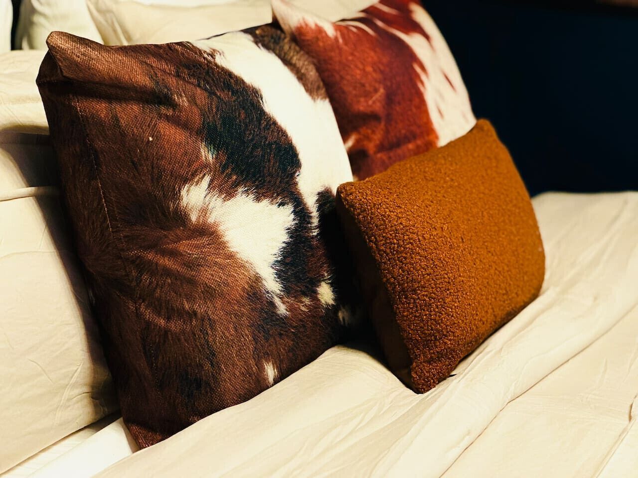 A bed with a white sheet and two pillows, one with a brown and white pattern and another plain brown.