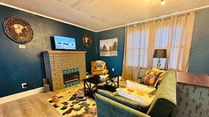 A living room with a brick fireplace, a green armchair, a wooden coffee table, and a patterned rug.