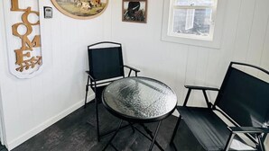 A room with a round glass table, two black chairs, a 'WELCOME' sign, a framed picture, and a window with a view of mountains.