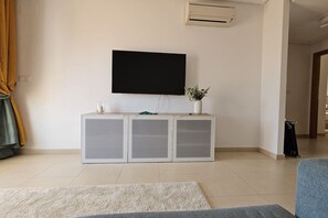 A living room with a flat-screen TV mounted on the wall, a white cabinet with glass doors, a small plant on top, and a grey sofa. - Very nice apartment at La Torre Golf Resort AO3711 (Murcia)