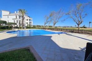 Una piscina con bordeado de baldosas, rodeada por una valla y árboles.