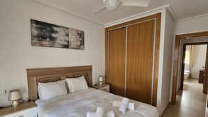 Ein Hotelzimmer mit einem Bett, einem Nachttisch, einer Lampe, einem Holzschrank und einem Deckenventilator.