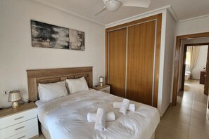 Habitación de hotel con cama, mesita de noche, lámpara, armario de madera y ventilador de techo.