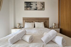 A neatly made bed with white linens and towels, a wooden headboard, bedside lamps, and a piece of abstract art on the wall. - Very nice apartment at La Torre Golf Resort AO3711 (Murcia)