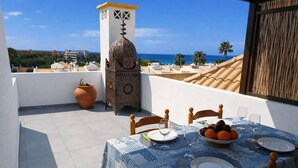 A terrace with a table set for two, a decorative tower, and a view of the sea. - T0 Condomínio jardim da Oura, A/c, piscinas, terra (Albufeira)