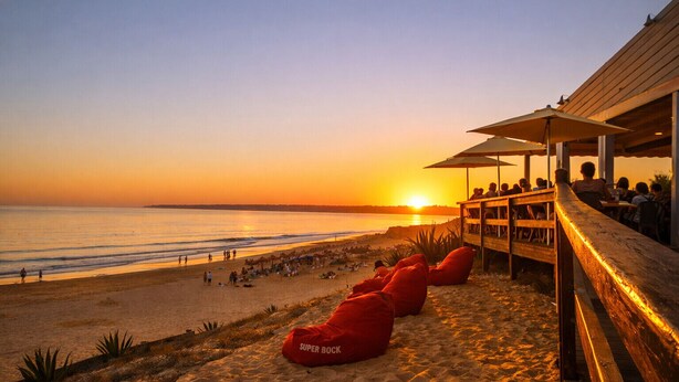 A beachside view with a wooden deck, red bean bags, and a sunset over the ocean. - T0 Condomínio jardim da Oura, A/c, piscinas, terra (Albufeira)
