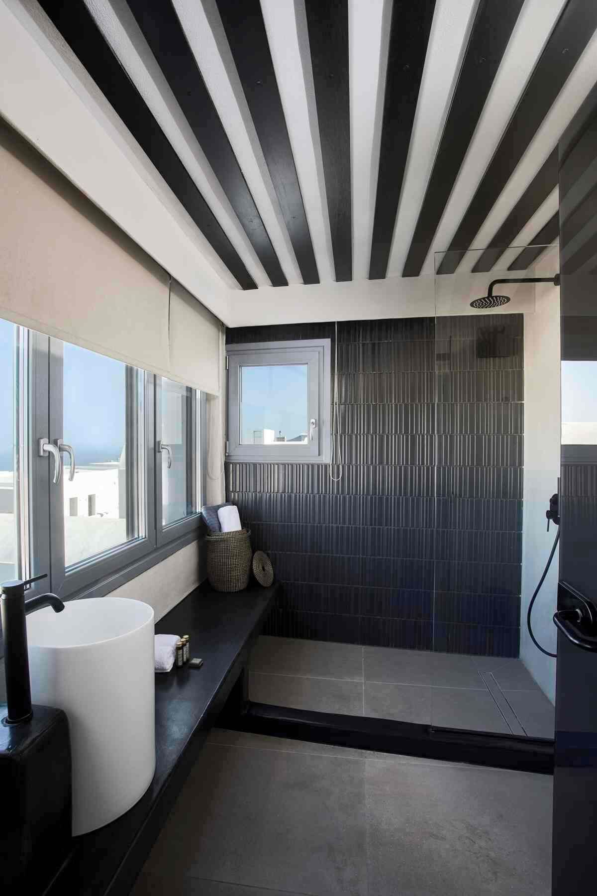 A modern bathroom with a large window, a shower, and a sink with a towel and basket.