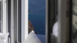 Vista desde una ventana con mar azul transparente y costa rocosa.