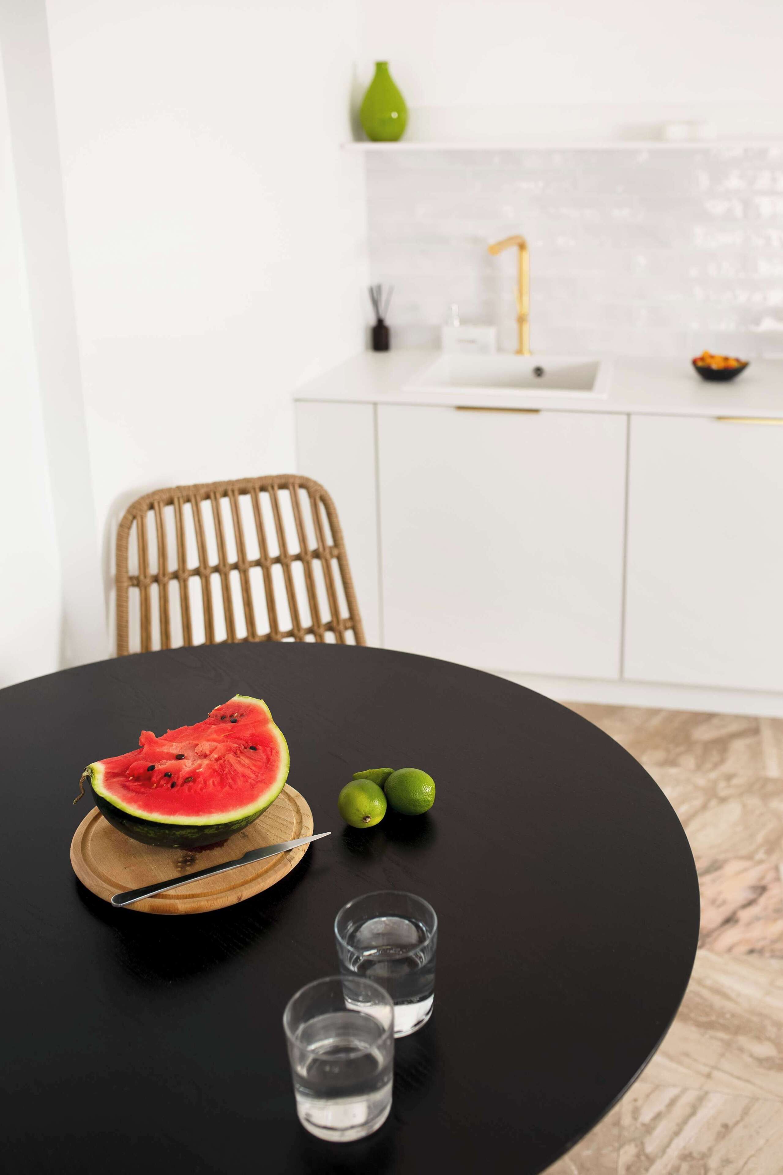 Une table à manger avec une pastèque, des citrons verts et deux verres d’eau.