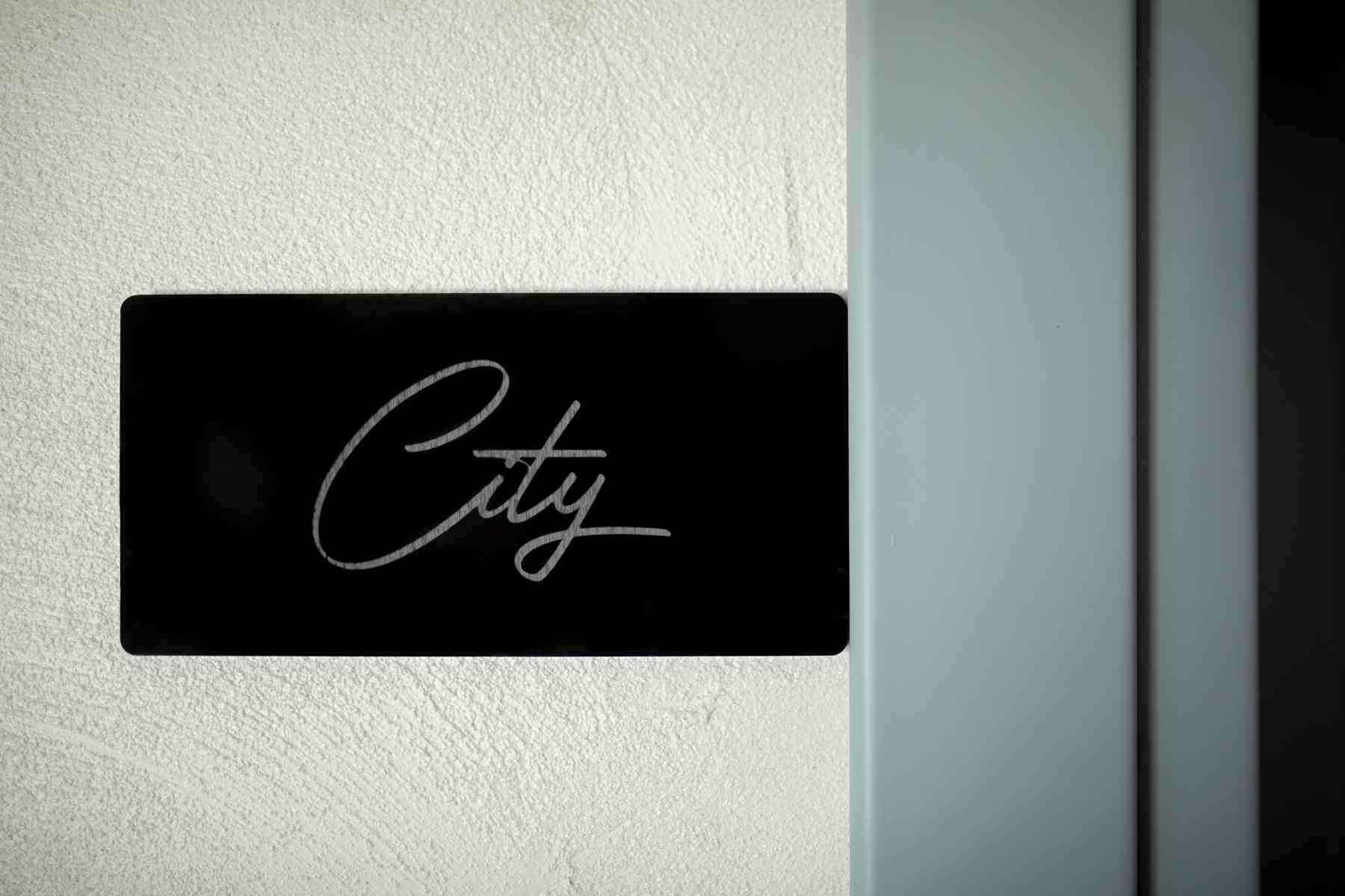 A black sign with the word "City" in cursive on a white wall.