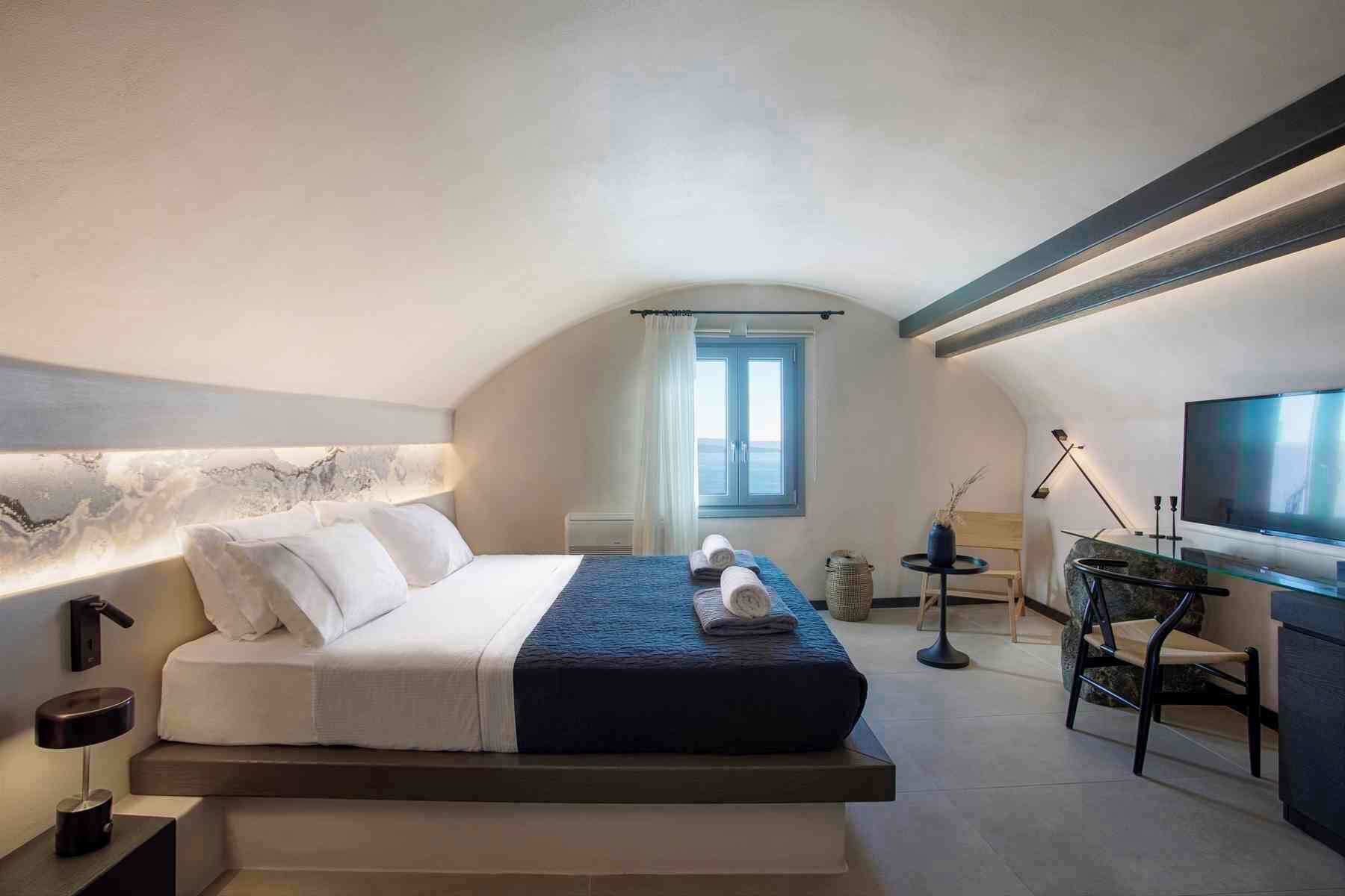 A modern bedroom with a bed, a desk, a chair, a television, and a window with curtains.