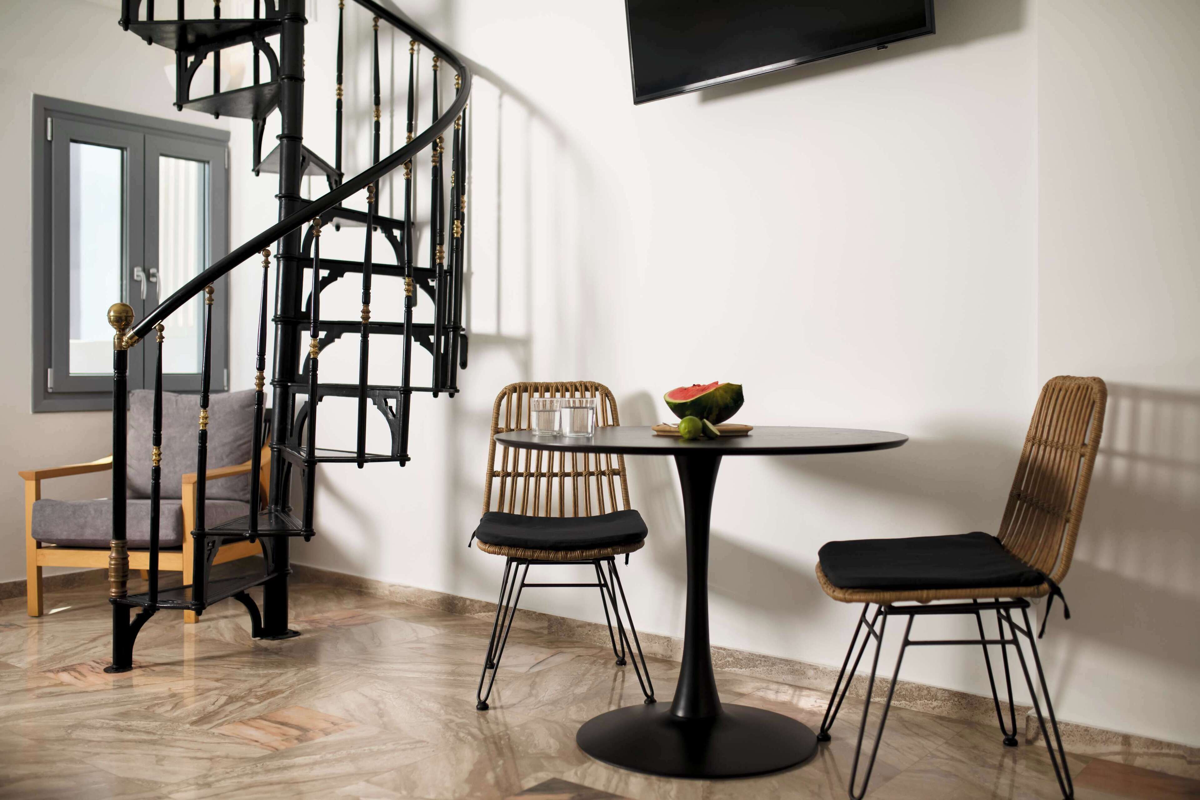 Een modern interieur met een spiltrap, een ronde tafel met twee stoelen en een aan de muur bevestigde televisie.