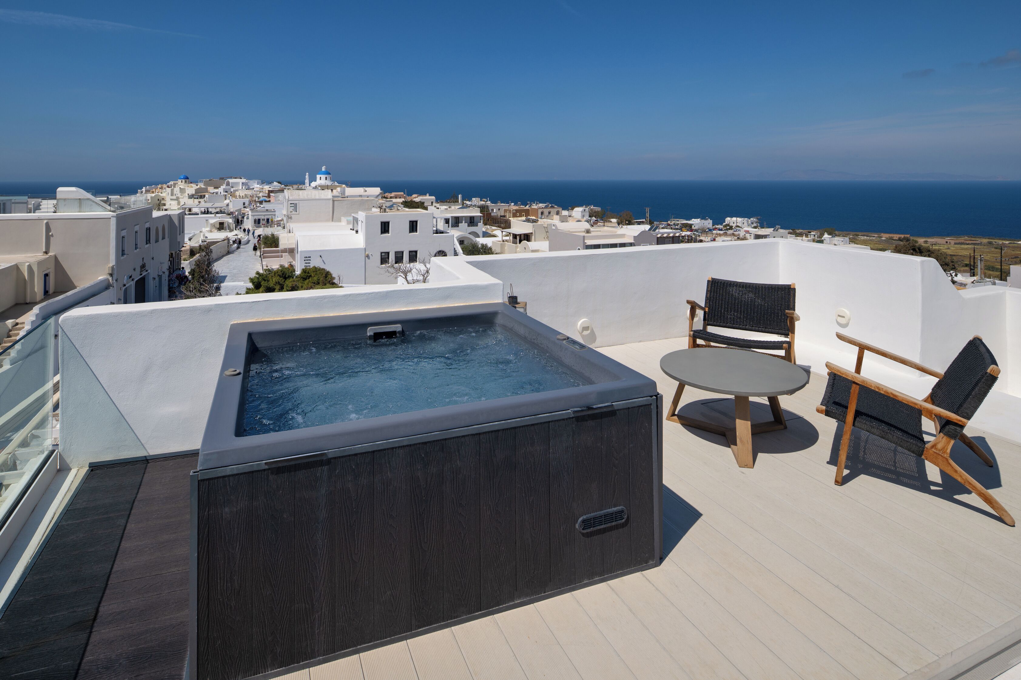 A rooftop terrace with a hot tub, two wicker chairs, and a table.