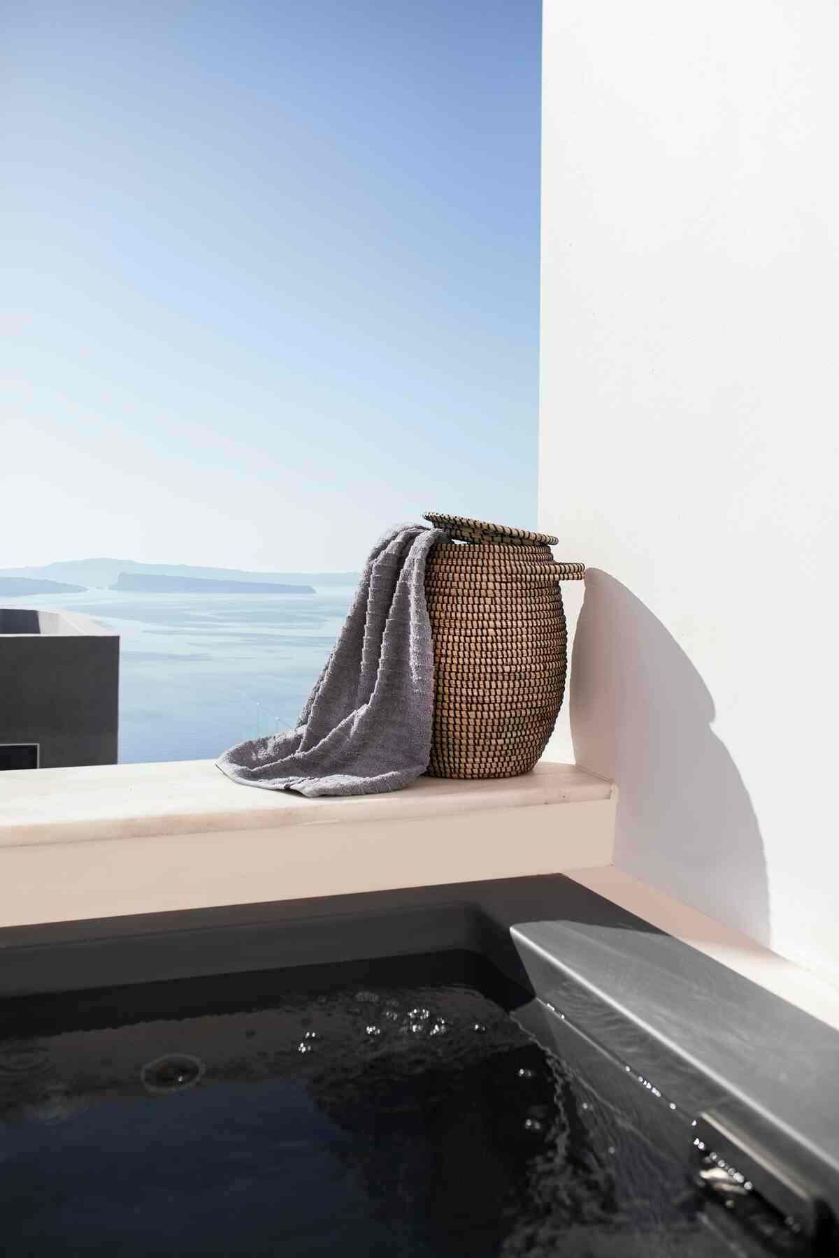 Una bañera con vista al mar, una toalla y una cesta de mimbre.
