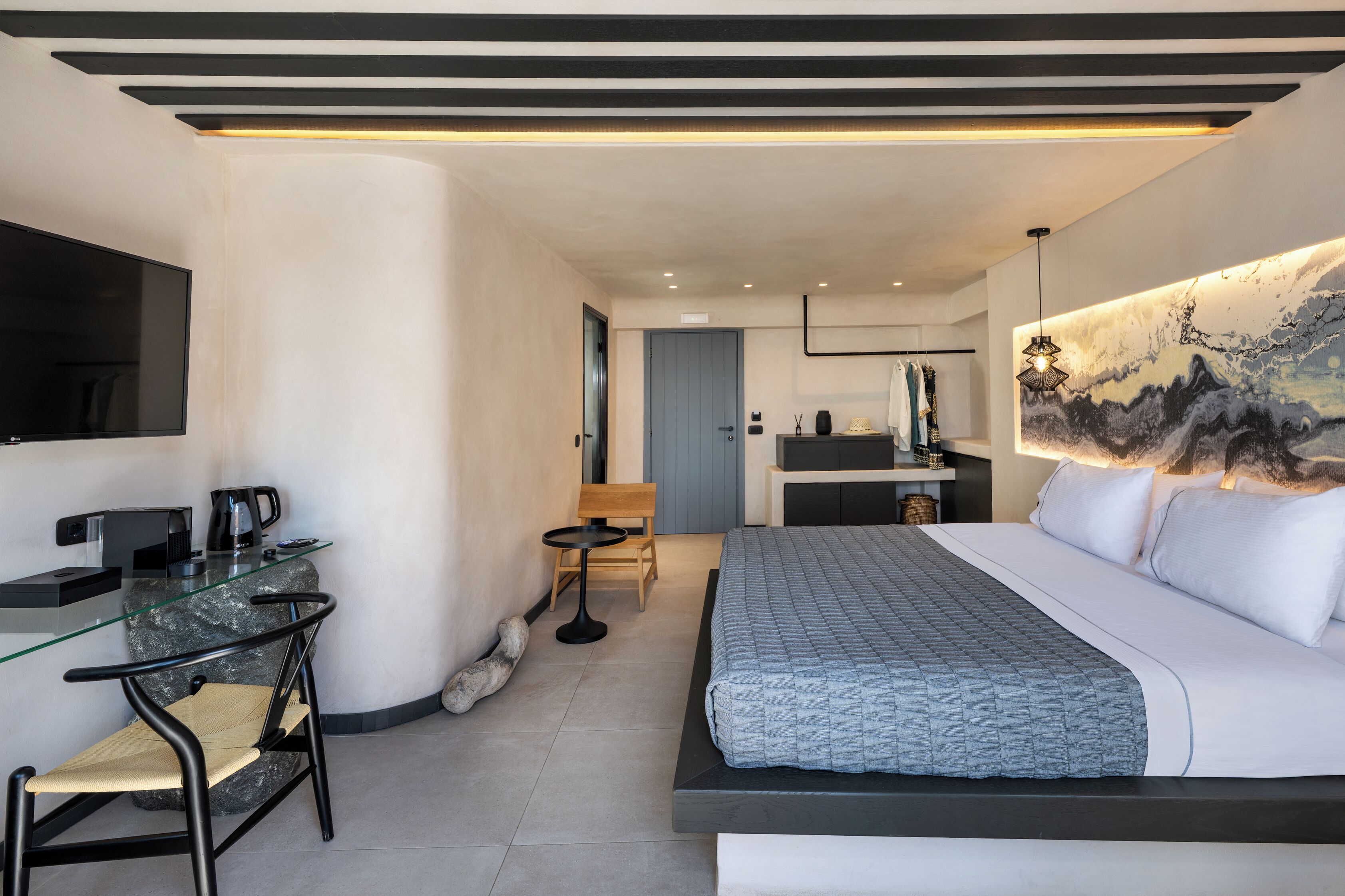 A modern hotel room with a bed, a desk, a chair, and a TV.