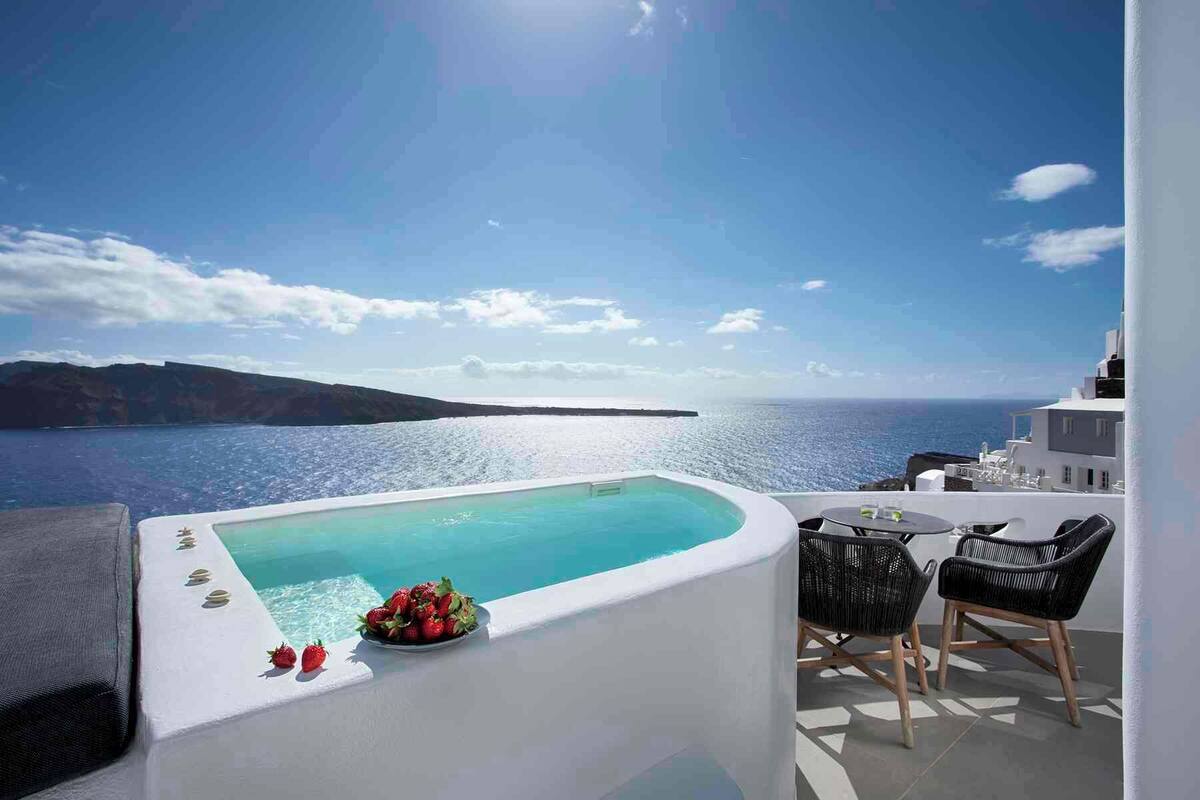 Une piscine sur le toit avec vue sur la mer et une île au loin, une petite table avec des chaises et une assiette de fraises.