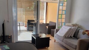Un salon moderne comprenant un canapé, une table basse et une table à manger. Une porte-fenêtre coulissante donne accès à un espace extérieur aménagé avec un salon de jardin.