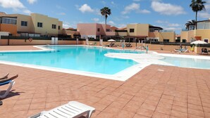 En swimmingpool med solstolar och parasoller, omgiven av höga byggnader med balkonger.