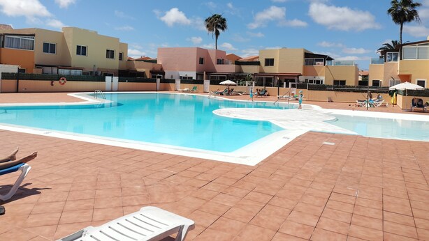 Une piscine entourée de bâtiments à plusieurs étages dotés de balcons, avec des chaises longues et des parasols à proximité.