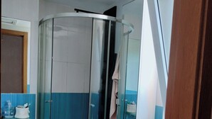 Une cabine de douche fermée par des parois de verre, avec une porte blanche, un mur recouvert de carreaux bleus et un lavabo blanc doté d’un distributeur de savon.