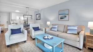 A modern living room with a light blue sofa, two armchairs, a coffee table, and a dining area with a table and chairs. - Tennis Villa D2 - 2BR Walk to Beach & Pool (Hilton Head Island)