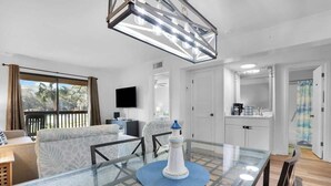 A modern living room with a glass dining table, a blue rug, and a white lighthouse decoration. - Tennis Villa D2 - 2BR Walk to Beach & Pool (Hilton Head Island)