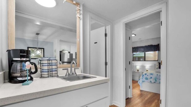A modern kitchen with a coffee maker, kettle, and a sink. There is a dining area with a table and chairs. - Tennis Villa D2 - 2BR Walk to Beach & Pool (Hilton Head Island)