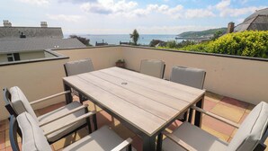 Ein Holztisch mit sechs Stühlen auf einer Terrasse mit Meerblick.