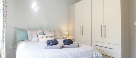 Un dormitorio con cama, almohadas, una mesita de noche, lámpara y armario.