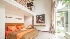A bedroom with a large bed, a chair, a shelf with decorative items, and a view of a swimming pool. - Swiss 2 Villa in Dalung (Tibubeneng)