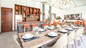 A modern dining area with a long wooden table set for six, surrounded by white chairs. - Swiss 2 Villa in Dalung (Tibubeneng)