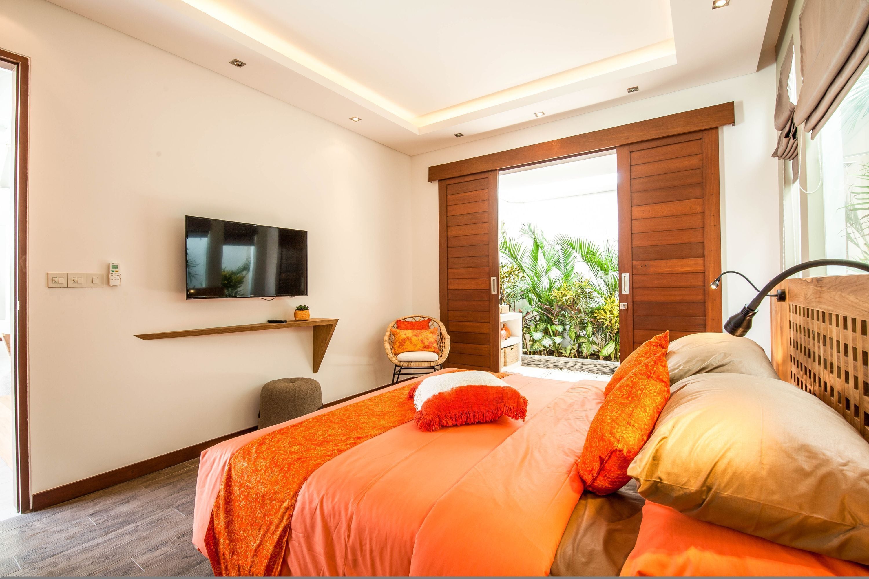 A modern bedroom with a large bed, a mounted TV, and a view of greenery outside.