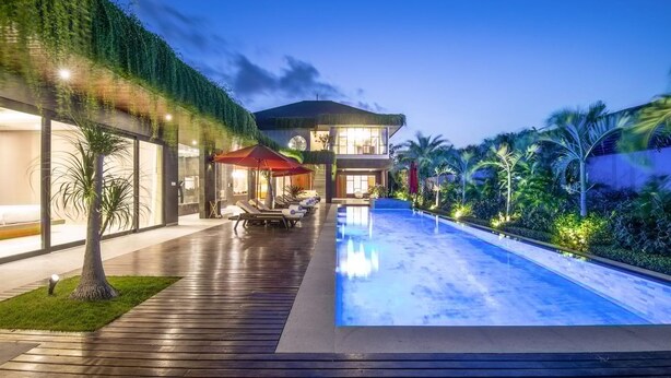 Una casa moderna con piscina, mobiliario exterior y exuberante vegetación.