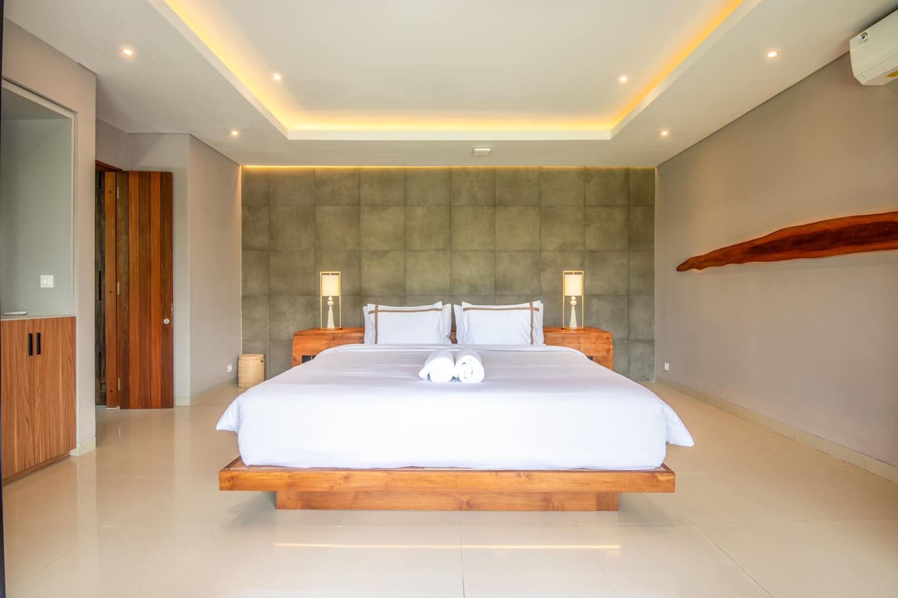 A modern bedroom with a large bed, wooden headboard, and two bedside lamps.