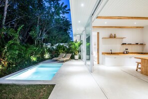 A modern house with a swimming pool, two lounge chairs, and a kitchen with white cabinets and wooden shelves. - ULU 3 2br Villa in Pecatu (Pecatu)
