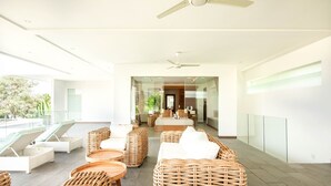 A modern, well-lit room with wicker furniture, a ceiling fan, and a glass partition leading to a bedroom. - Niko 2 R New Villa Close to Finns Beach Club (Canggu)