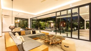 A modern living room with a glass coffee table, a sofa, and a large window overlooking a pool area. - Niko 2 R New Villa Close to Finns Beach Club (Canggu)