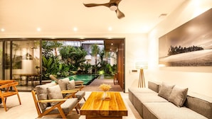 A modern living room with a wooden coffee table, sofas, and chairs. There is a pool visible through the glass doors. - Noma 5 Victum in Pererenan (Pererenan)