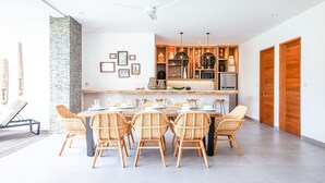 Een moderne eetruimte met een lange tafel en rieten stoelen, een keuken met houten kasten en hanglampen, en een accentmuur van steen.