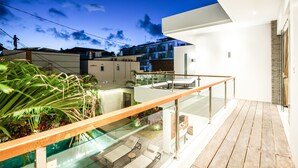 Een modern buitenverblijf met glazen balustrade, houten terras en lounge fauteuils.