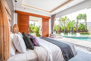 Quarto moderno com uma cama grande, porta de madeira e vista para uma piscina e plantas tropicais.