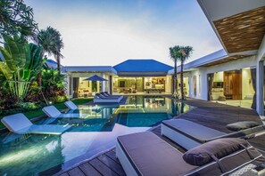 Uma casa moderna com piscina, espreguiçadeiras e um jardim bem cuidado.