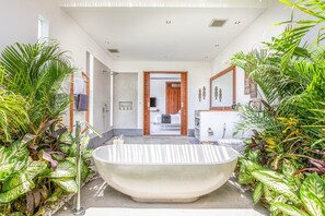 Um banheiro moderno com uma banheira livre e cercado por plantas tropicais exuberantes.