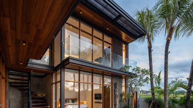 Et moderne hus med to etager, en glasfacade, træterrasse og swimmingpool.