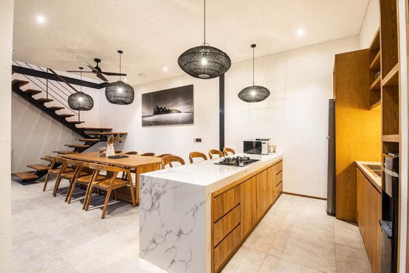 A modern kitchen with a marble island, wooden cabinetry, and pendant lighting. - Noma 6 Dollar in Pererenan (Munggu)