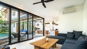 Ein modernes Wohnzimmer mit Couchtisch aus Holz, dunklen Sofas und einer Glaswand mit Blick auf einen Pool und eine Außenbereichs-Sitzgruppe.