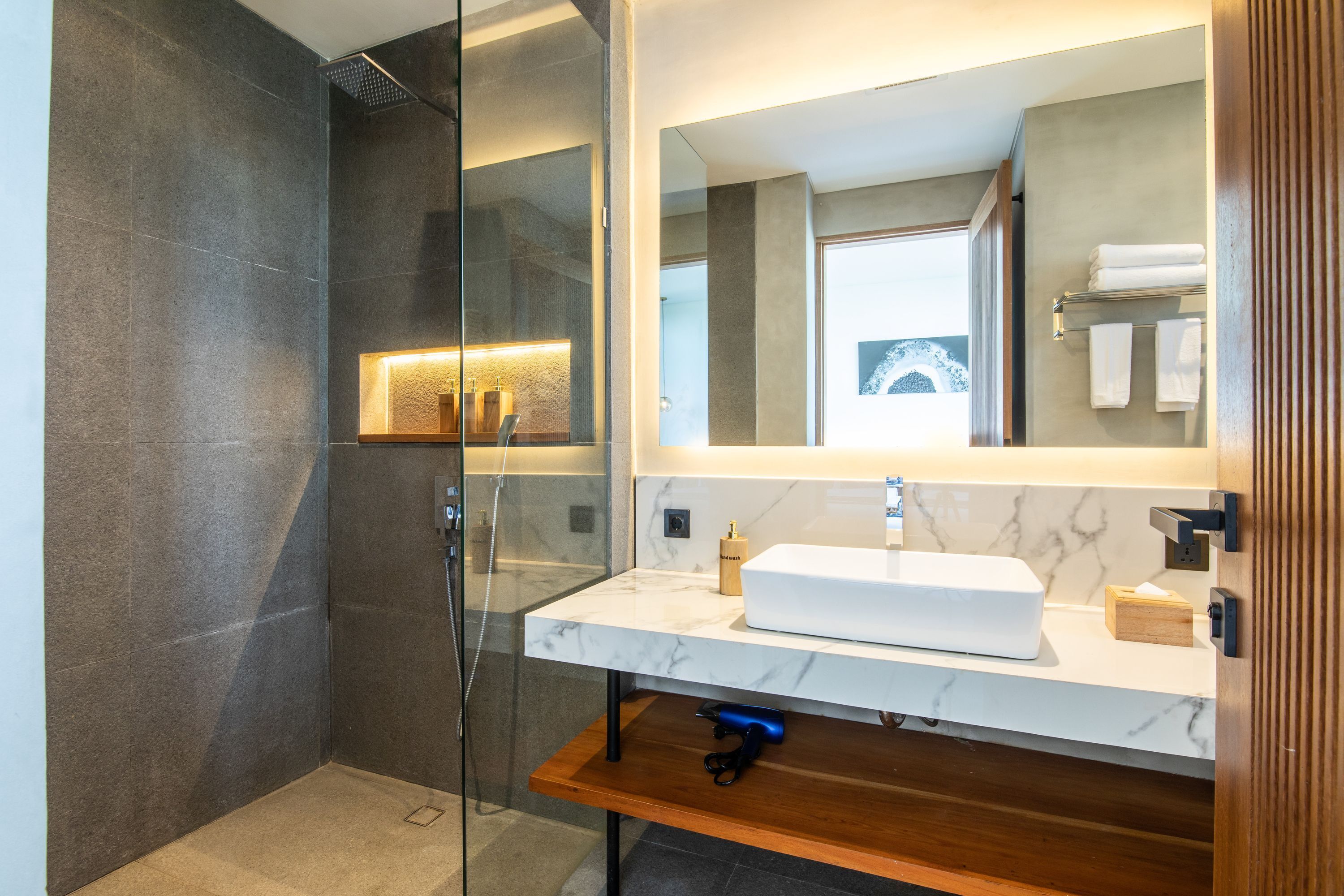 A modern bathroom with a glass shower enclosure, a marble sink, and a wooden vanity.